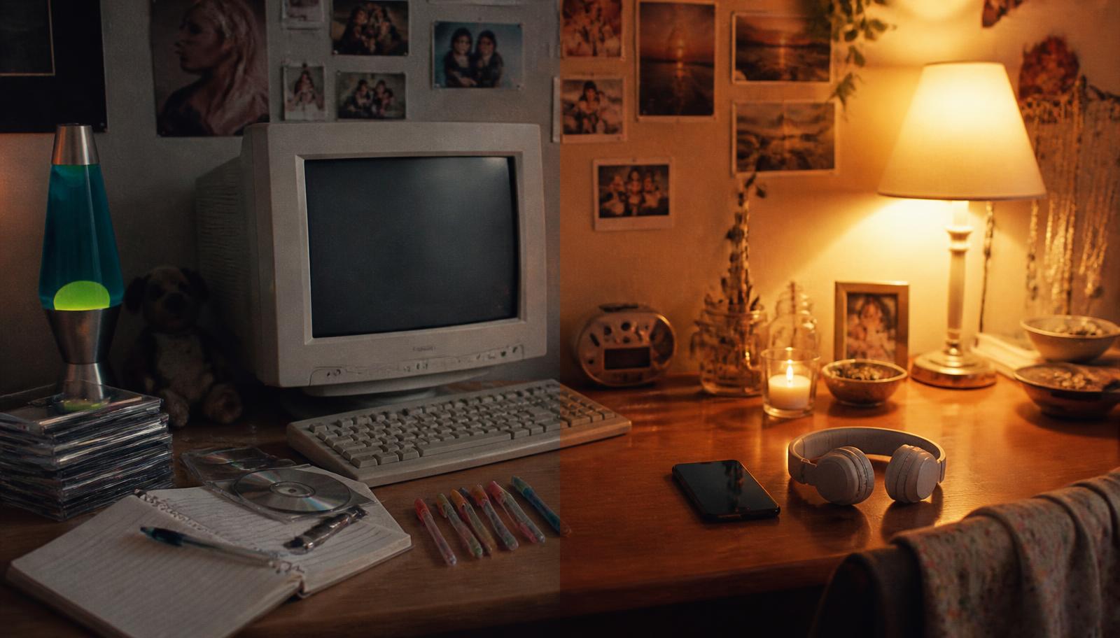 A desk split between a retro computer with CDs and gel pens and a modern phone with headphones